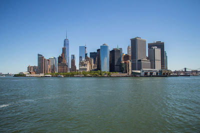 Sea by cityscape against clear blue sky