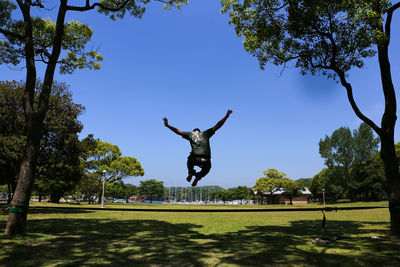 Rear view of man jumping with arms outstretched over rope at park