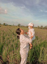 Mother carrying daughter while standing on grassy landscape