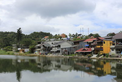 Houses by lake and buildings against sky