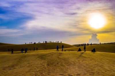 People on desert against sky during sunset