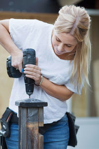 Happy woman using cordless screwdriver on wooden post