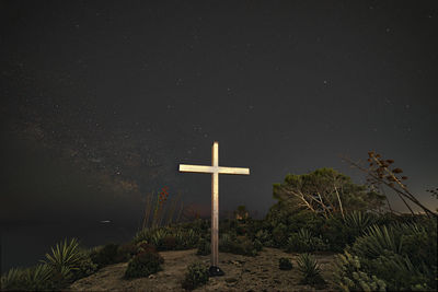 Low angle view of cross amidst trees against sky at night