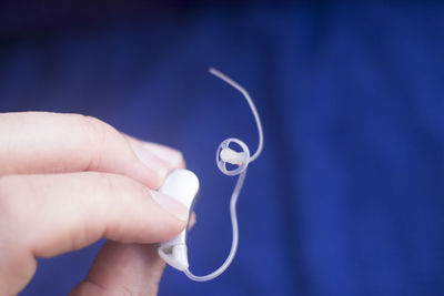 Close-up of person holding hearing aid against blue background