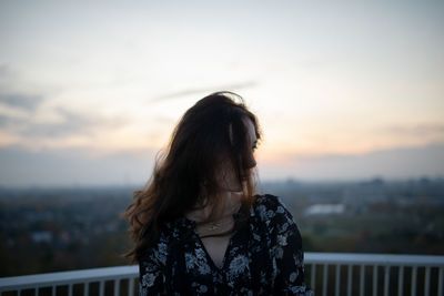 Woman looking at cityscape against sky during sunset