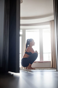 Side view of woman sitting on window