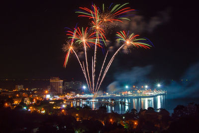 Firework display over illuminated city against sky at night