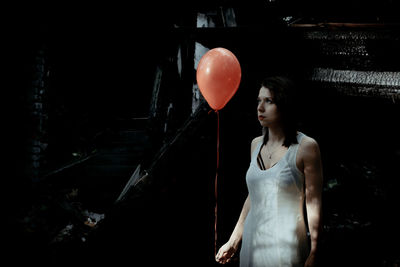 Woman holding helium balloon while standing at forest