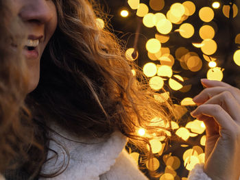 Close-up of happy woman against christmas lighting