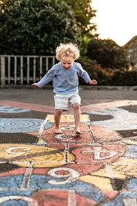 Happy toddler boy in mid-jump playing hopscotch