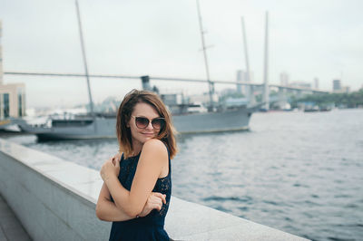 Portrait of young woman wearing sunglasses standing on car