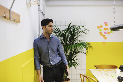 Thoughtful young man leaning on wall in creative office