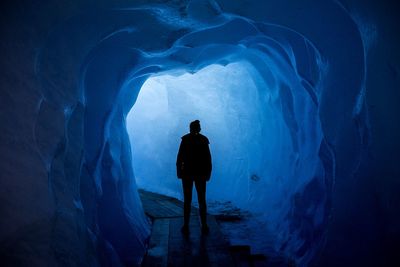 Rear view of silhouette woman standing in ice cave tunnel