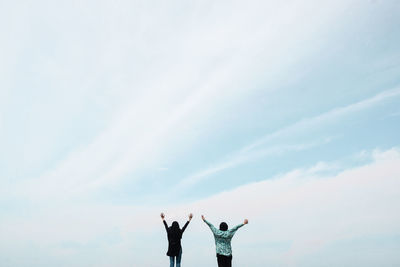 Rear view of friends with arms raised standing against sky