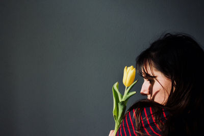 Woman holding flower against gray wall