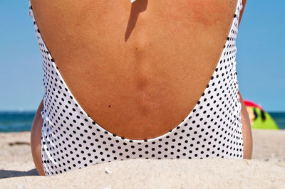 Rear view of woman siting on sand at beach against sky