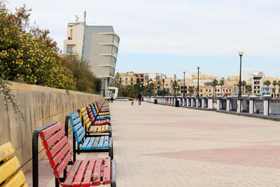 Man walking on footpath by building against sky