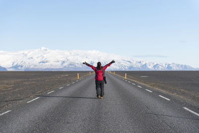 Rear view full length of woman standing against snowcapped mountains on road