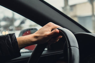 Selective focus man's hand on steering wheel, driving car in winter background. travel background