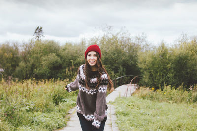 Portrait of smiling young woman standing on footpath against trees and plants