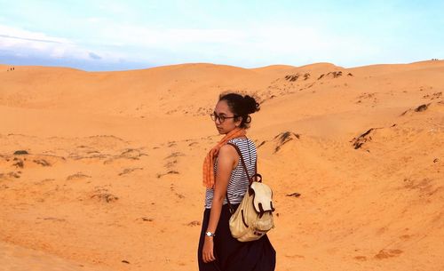 Rear view of woman standing at red sand dunes against sky