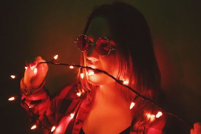 Close-up portrait of young woman holding illuminated lighting equipment