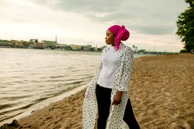 Young woman standing at beach against sky