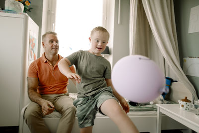 Man sitting behind boy with down syndrome playing with balloon