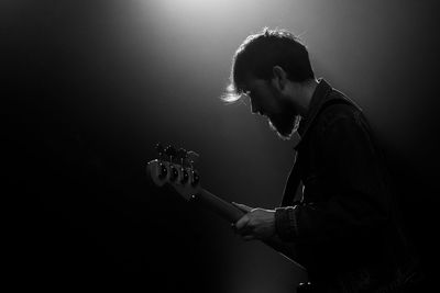 Side view of man playing guitar against black background