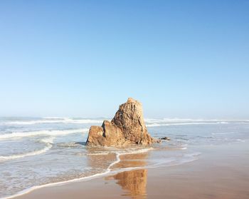 Rock formation on beach against clear blue sky