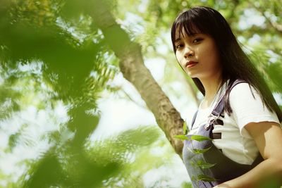 Portrait of young woman standing against tree