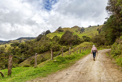 Rear view of man walking on dirt road against mountains