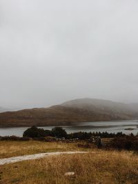 Scenic view of field by lake against sky