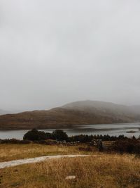 Scenic view of field by lake against sky