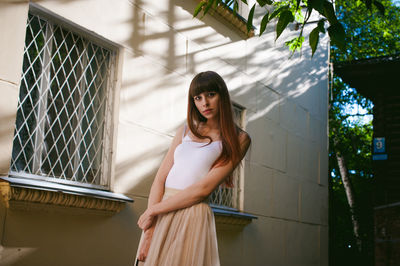 Portrait of young woman standing against building