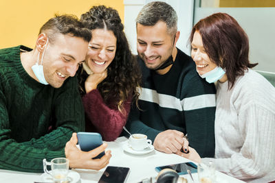 Cheerful friends looking at mobile phone while sitting at cafe