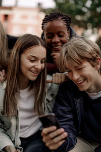 Smiling teenage boy showing smart phone to friends friends at park