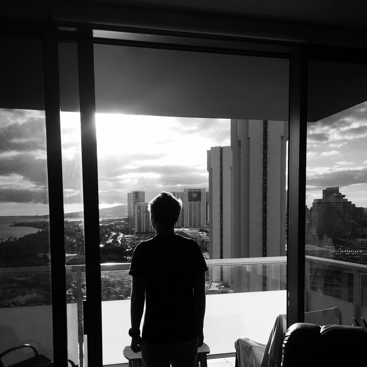 rear view, sky, window, indoors, built structure, architecture, men, glass - material, looking at view, city, lifestyles, standing, cloud - sky, building exterior, transparent, looking through window, cloud, cityscape