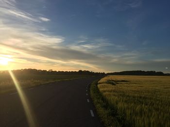 Road amidst field against sky during sunset