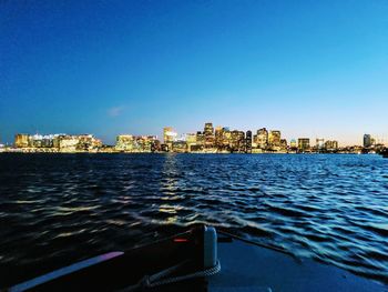 Buildings by sea against clear blue sky