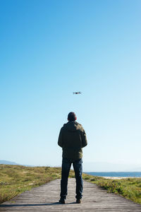 Young man flying a dron near to the beach backwards