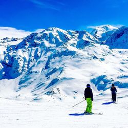 Rear view of people skiing on snowcapped mountain against sky