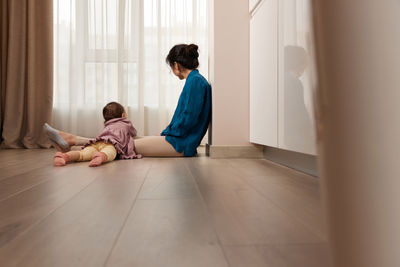Side view of woman sitting on hardwood floor at home