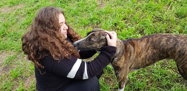 Side view of woman pampering dog on grassy field