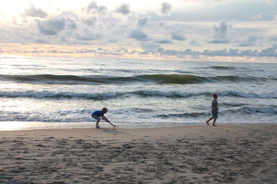 Man surfing on beach against sky during sunset