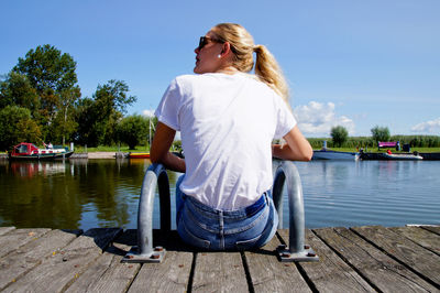 Rear view of young woman sitting on pier over lake