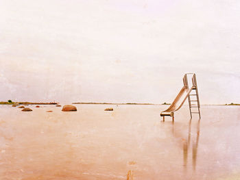 Old steel slide in lake. chrome ladder tower with sliding track, big granite stones around. smooth 