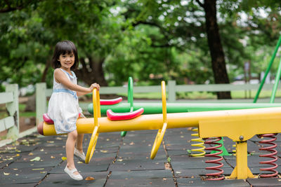 Portrait of smiling girl sitting on seesaw in playground