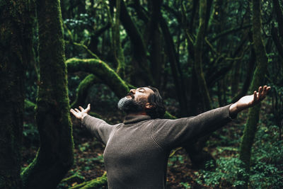 Low angle view of man with arms outstretched standing in forest