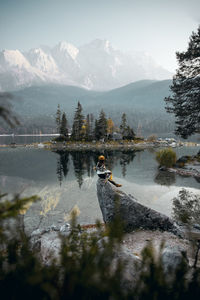 Woman sitting on rock over lake against mountains and sky